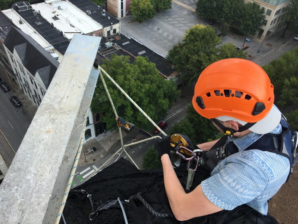 A technician at an engineering firm performing a building envelope inspection while connected to a safety harness.